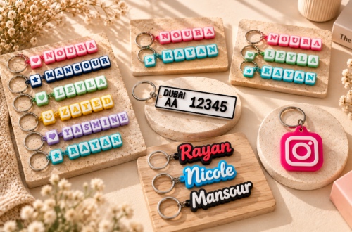 Flat lay of Forjolie personalized keychains including a UAE-style license plate keychain, an Instagram NFC tag keychain, and custom wood name keychains reading Nicole and Maroun