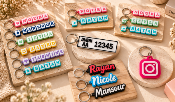 Flat lay of Forjolie personalized keychains including a UAE-style license plate keychain, an Instagram NFC tag keychain, and custom wood name keychains reading Nicole and Maroun